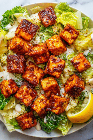 Crispy Buffalo Tofu served on a refreshing Caesar salad with lemon wedges, ideal for festive gatherings and plant-based meals.