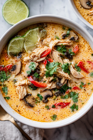 A bowl of Thai Coconut Chicken Soup filled with chicken, mushrooms, and vibrant vegetables, perfect for cold days and holiday meals.