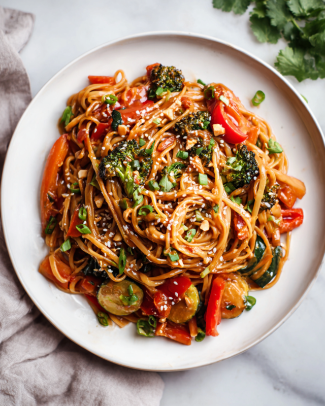 Bowl of peanut noodles with colorful roasted vegetables, garnished with scallions and sesame seeds, perfect for weeknight dinners and potlucks.